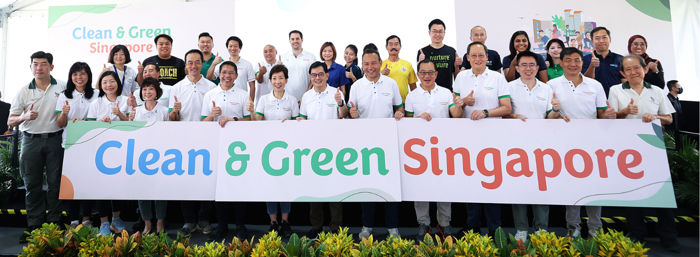 Group holding "Clean & Green Singapore" sign, giving thumbs up.